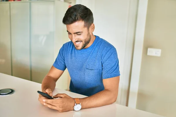 Evdeki Masada Oturan Akıllı Telefonu Kullanarak Mutlu Gülümseyen Genç Adam — Stok fotoğraf