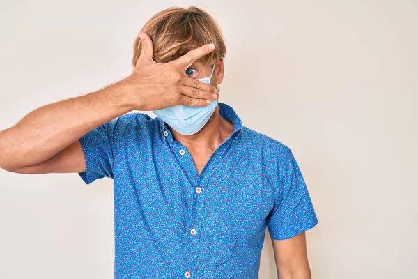 Young Blond Man Wearing Medical Mask Peeking Shock Covering Face — Stock Photo, Image