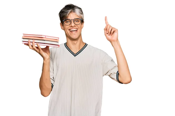 Young Hispanic Man Holding Books Surprised Idea Question Pointing Finger — Stock Photo, Image