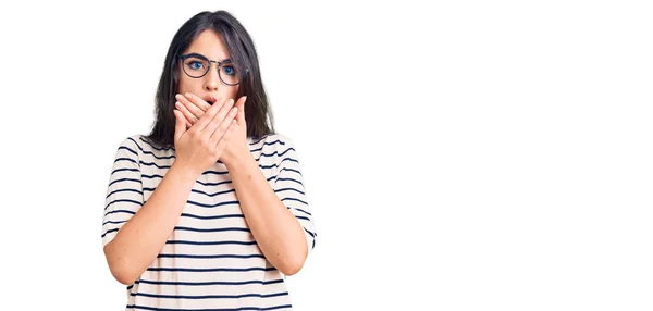 Brunetka Nastolatka Luźnych Ubraniach Okularach Zszokowana Zakrywając Usta Rękami Przez — Zdjęcie stockowe