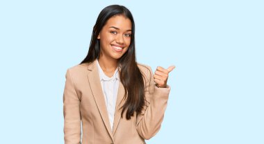 Güzel İspanyol kadın, iş ceketi giyiyor, gülümsüyor, gülümsüyor ve başparmağıyla yan tarafa bakıyor.. 