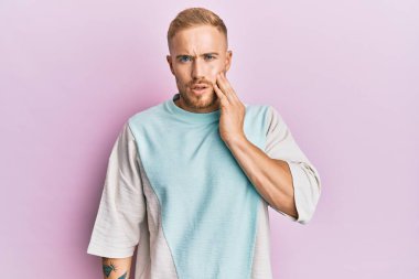 Günlük kıyafetler giyen genç beyaz bir adam diş ağrısı ya da diş hastalığından dolayı acı dolu bir ifadeyle ağıza dokunuyor. dişçi 