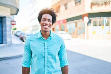 Genç, yakışıklı, Afro-Amerikan bir adam günlük giysiler giyip mutlu gülümsüyor. Yüzünde gülümsemeyle kasaba caddesinde yürürken.