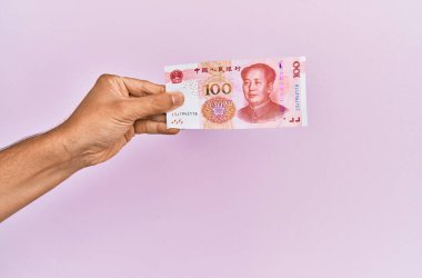İspanyol eli 100 Yuan 'lık Çin banknotunu soyutlanmış pembe arka planda tutuyor..