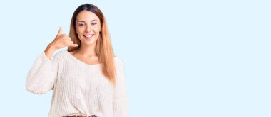 Güzel, genç bir kadın günlük kıyafetler giyip gülümsüyor telefonla el ve parmaklarıyla jest yapıyor telefonda konuşuyor gibi. iletişim kavramları. 