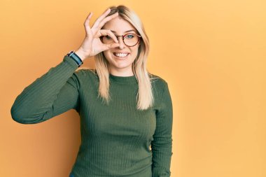 Gündelik giysiler ve gözlük takan genç beyaz kadın el hareketleriyle gülümsüyor, gözleriyle mutlu yüzle parmaklarının arasından bakıyor.. 