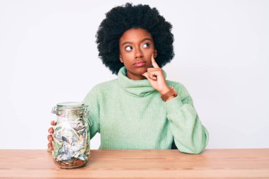Genç Afrikalı Amerikalı kadın elinde kavanozla ciddi bir yüz ifadesiyle el pençe divan sorular soruyor, kafa karıştırıcı bir fikir. 