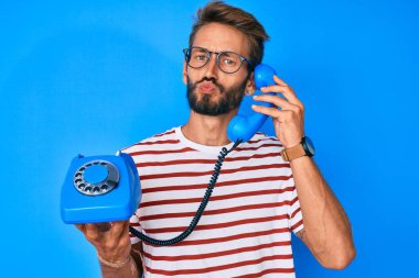 Yakışıklı, beyaz, sakallı, antika bir telefon tutan ve kameraya bakıp öpüşen sevimli ve seksi bir adam. aşk ifadesi. 