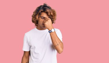 Gündelik beyaz tişört giyen genç İspanyol adam yorgun burnu ve gözleri ovuşturup yorgunluk ve baş ağrısı hissediyor. Stres ve hüsran kavramı. 