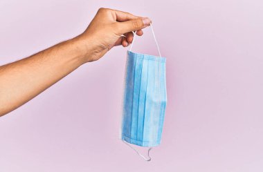 İzole edilmiş pembe arka planda tıbbi maske tutan İspanyol bir adam..