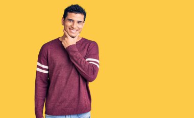 İspanyol asıllı yakışıklı genç adam gündelik kıyafetler giyiyor kameraya bakıyor kollarını kavuşturup gülümsüyor ve çenesini kaldırıyor. Olumlu düşünmek. 