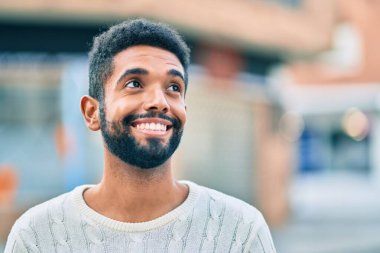 Genç Afrikalı Amerikalı adam gülümseyerek şehirde mutlu mesut duruyor..