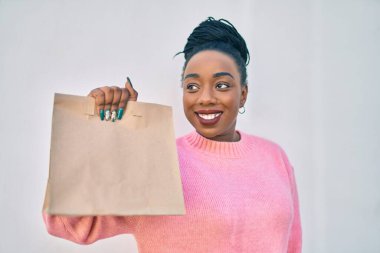 Genç Afro-Amerikalı kadın gülümseyerek elinde kağıt torbayla şehirde yiyecek taşıdığını söylüyor..