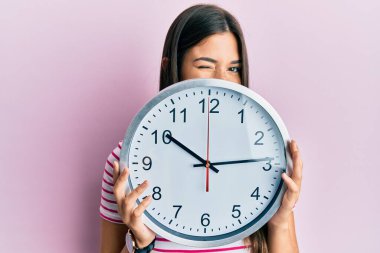 Genç esmer kadın büyük bir saat tutuyor yüzünü kapatıyor kameraya seksi bir ifadeyle bakıyor, neşeli ve mutlu bir yüzle.. 