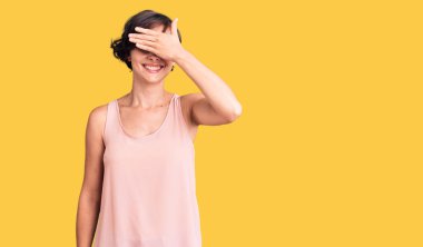 Kısa saçlı, sıradan giyinen, kolsuz tişörtlü, gülümseyen ve yüzünde şaşkınlık için gözleri kapayan güzel bir genç kadın. kör kavram. 