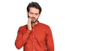 Günlük kıyafetler giyen genç İspanyol adam diş ağrısı ya da diş hastalığından dolayı acı dolu bir ifadeyle ağıza dokunuyor. dişçi 