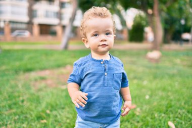 Sevimli ve mutlu küçük çocuk güneşli bir günde parkta eğleniyor. Güzel sarı saçlı erkek çocuk dışarıda oynuyor.