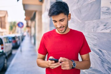 Genç Latin adam mutlu bir şekilde gülümsüyor ve şehirde akıllı telefon kullanıyor..