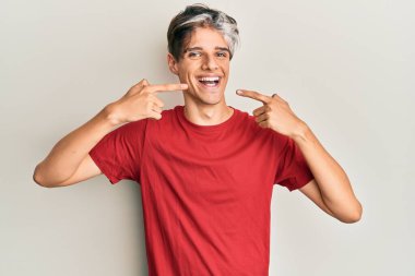 Günlük kıyafetler giyen, neşeli gülümseyen, parmaklarıyla ve ağzıyla işaret eden İspanyol genç bir adam. diş sağlığı kavramı. 