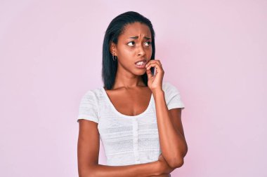 Rahat kıyafetler giyen genç Afro-Amerikalı kadın gergin ve gergin görünüyor. Ağzı tırnak yiyen ellerle. anksiyete. 