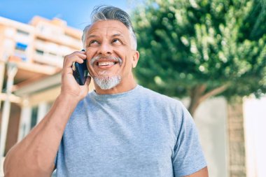 Orta yaşlı, İspanyol, gri saçlı, gülümseyen, mutlu, akıllı telefondan konuşan bir adam..