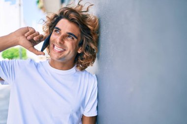 Duvara yaslanmış akıllı telefondan konuşan genç İspanyol bir adam.