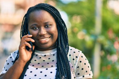 Genç Afrikalı Amerikalı kadın gülümsüyor. Şehirdeki akıllı telefondan mutlu bir şekilde konuşuyor..