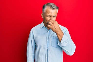 Orta yaşlı, gri saçlı, günlük kıyafetler giyen, pis ve iğrenç bir koku alan, nefesini burnunda tutan bir adam. Kötü kokuyor. 