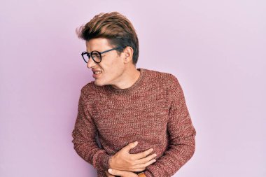 Yakışıklı, beyaz bir adam günlük süveter giyiyor ve eli karnında gözlük takıyor çünkü mide bulantısı, acı verici bir hastalık kendini iyi hissetmiyor. Ağrı kavramı. 