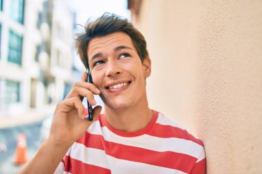 Genç beyaz adam gülümsüyor. Şehirdeki akıllı telefondan konuşuyor..