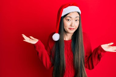 Genç Çinli kadın noel şapkası takıyor, habersiz ve kolları açık, hiçbir fikrim yok ve şüpheli bir yüz var.. 