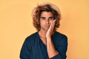 Yazlık şapkalı genç İspanyol adam çapraz kollu depresyondan sıkılmış ve yorgun görünüyor.. 