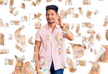 Yakışıklı Latin Amerikalı, günlük tişört giyen, gülümseyen, el ve parmaklarıyla 