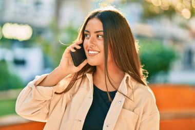 Genç İspanyol kız gülümsüyor. Parktaki akıllı telefondan konuşarak mutlu oluyor..