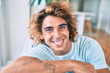 Evdeki kanepede mutlu gülümseyen İspanyol genç adam.