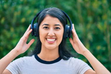 Genç İspanyol kadın gülümseyerek şehirde kulaklık takarak müzik dinliyor..