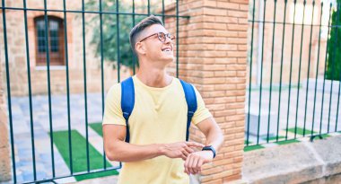 Genç İspanyol öğrenci mutlu bir şekilde gülümsüyor. Şehrin caddesindeki saati işaret ediyor.