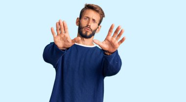 Sakallı, sıradan bir süveter giyen yakışıklı sarışın. Avuç içi hareketlerini durduruyor. Öfkeli ve hayal kırıklığı dolu bir ifade takınıyor. 