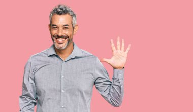 Orta yaşlı, gri saçlı, günlük kıyafetler giyen, beş numaralı parmaklarıyla işaret eden, kendinden emin ve mutlu bir adam.. 