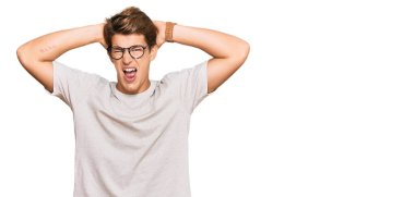 Yakışıklı beyaz bir adam günlük kıyafetler ve gözlük takıyor çılgın ve elleri başında korkmuş, ağzı açık şoktan korkmuş ve şaşırmış. 