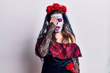 Young woman wearing day of the dead costume over white yawning tired covering half face, eye and mouth with hand. face hurts in pain. 