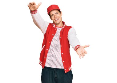 Beyzbol üniforması giyen yakışıklı beyaz adam kameraya sarılıp gülümsüyor. Mutluluğu kucaklayan neşeli bir ifade.. 