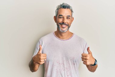 Orta yaşlı, gri saçlı, günlük kıyafetler giyen, başarı işareti takan, elinde olumlu bir jest yapan, gülümseyen ve mutlu bir adam. Neşeli ifade ve kazanan jest. 