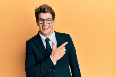 Yakışıklı, beyaz takım elbiseli ve kravatlı. Yüzünde mutlu ve doğal bir ifadeyle, elleri ve parmaklarıyla yüzünü gösteren bir gülümseme. 