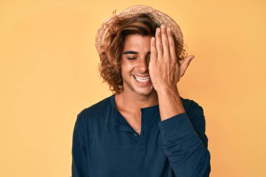 Yaz şapkası takan genç İspanyol bir adam bir gözünü eliyle kapatıyor, yüzünde kendine güvenen bir gülümseme ve şaşırtıcı bir duygu var.. 