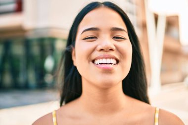 Genç Asyalı kız şehirde mutlu bir şekilde gülümsüyor.