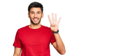 Kırmızı tişört giyen genç ve yakışıklı bir adam dört numarayı gösterip işaret ederken kendinden emin ve mutlu gülümsüyor.. 