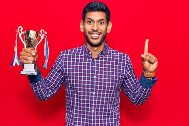 Genç Latin adam elinde kupa tutarken bir fikir ya da soruyla gülümsüyor ve mutlu bir yüzle işaret ediyor. 