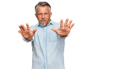 Orta yaşlı, gri saçlı, günlük kıyafetler giyen, avuç içi hareketlerini durduran, sinirli ve hayal kırıklığına uğramış bir adam. 