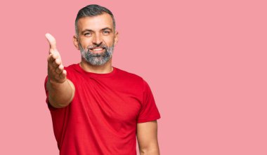 Orta yaşlı, sıradan kıyafetler giyen yakışıklı bir adam dostça bir selamlama ve hoş geldin hediyesi olarak el sıkışmayı sunuyor. başarılı iş. 